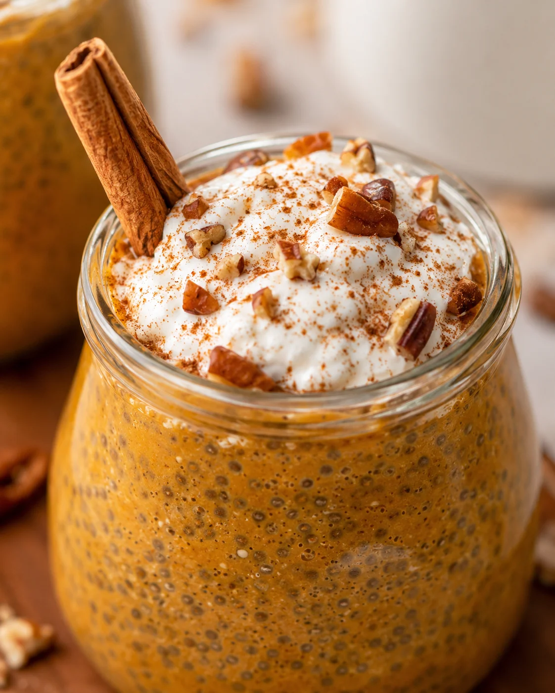 Creamy pumpkin chia pudding topped with nuts and a cinnamon stick.
