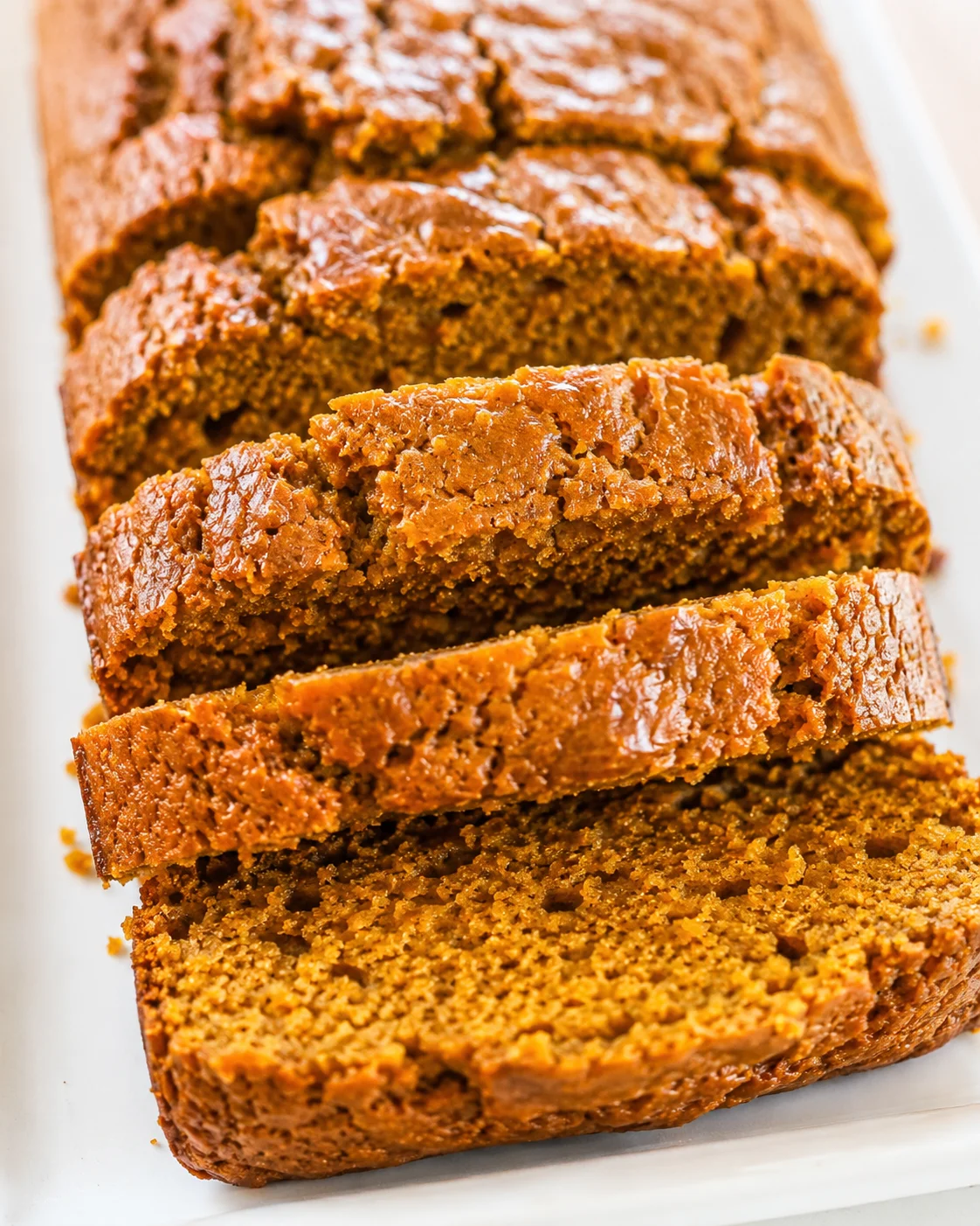 Close-up of sliced vegan pumpkin applesauce bread showing crust and crumb on a white surface