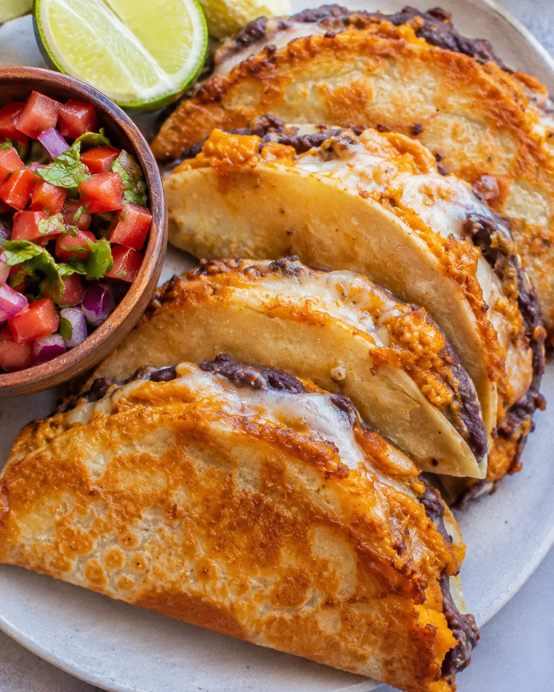 Plate of pumpkin and black bean tacos with melted cheese, pico de gallo, and lime wedges