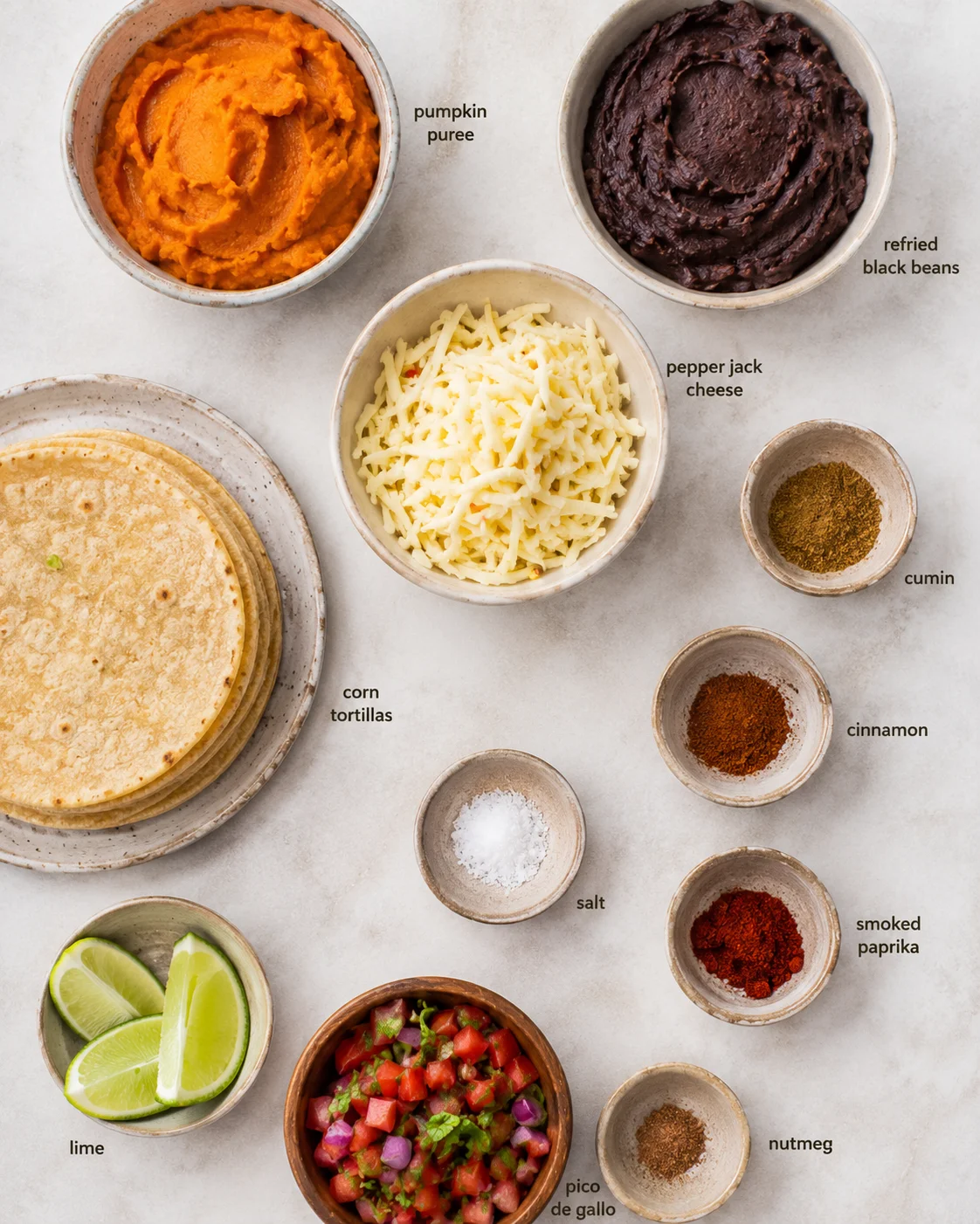 Top-down arrangement of pumpkin puree, refried black beans, cheese, corn tortillas, spices, lime and pico de gallo