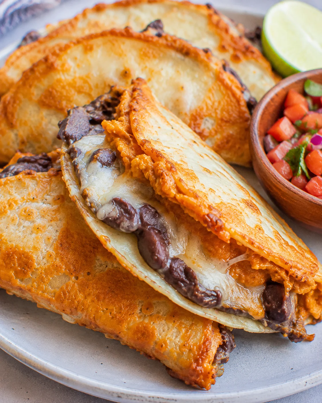 Side view of crispy pumpkin and black bean tacos showing melted cheese and browned tortilla edges