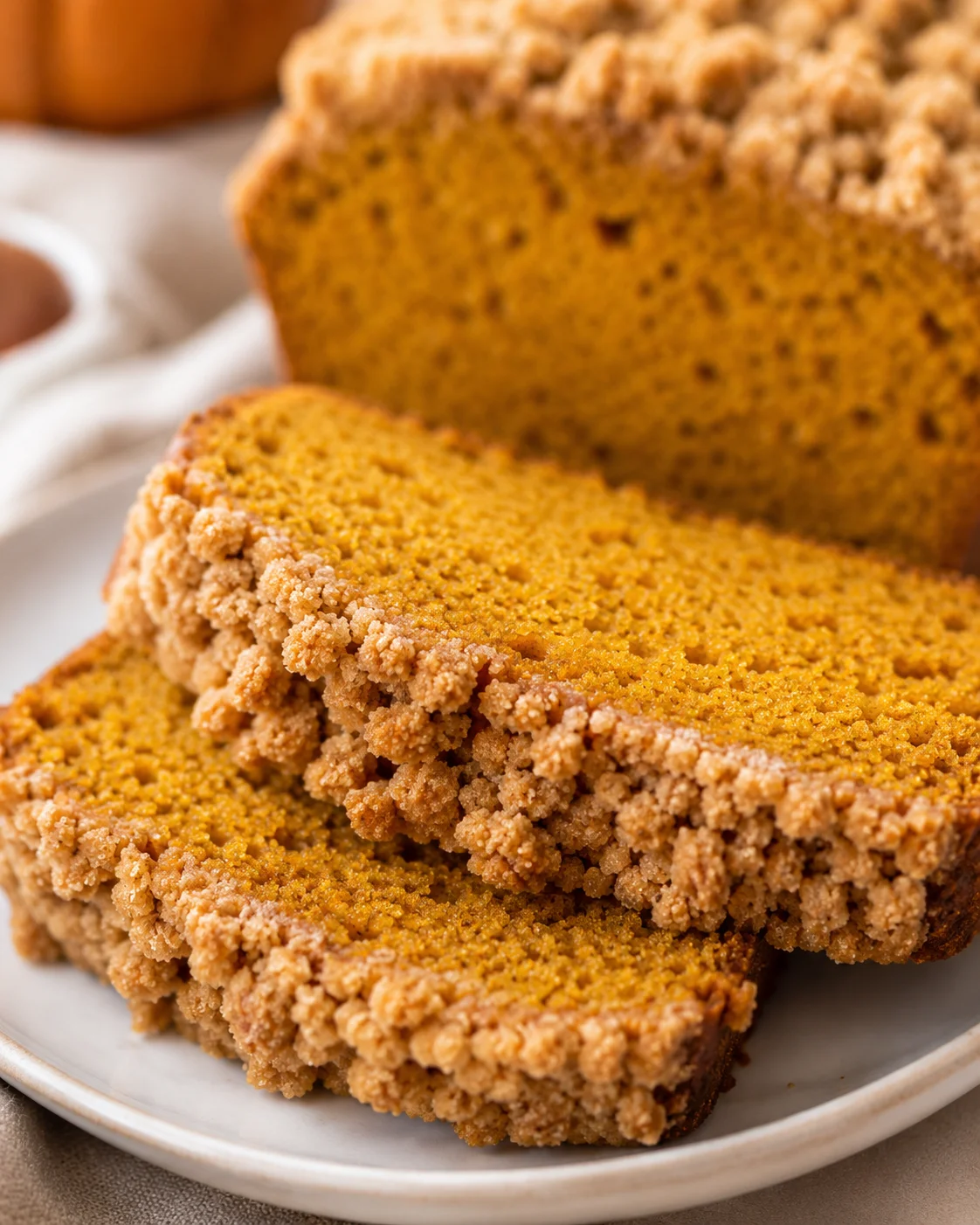 Two slices of pumpkin bread with crumb topping on a plate and the remaining loaf in background