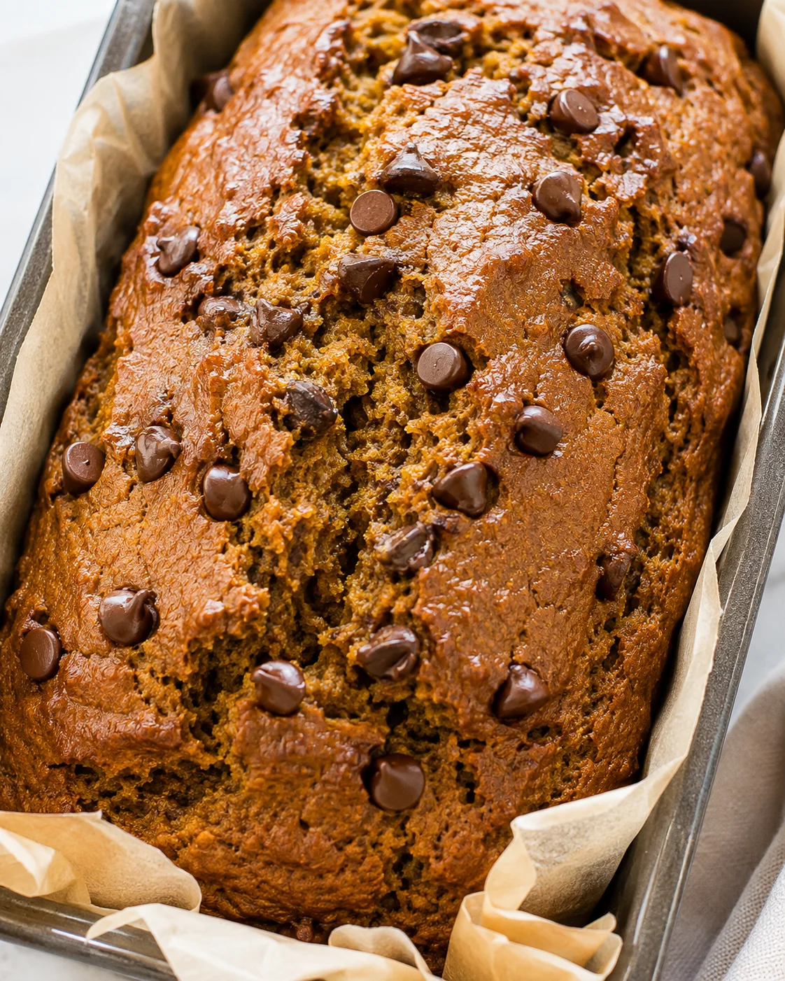 Pumpkin chocolate chip bread loaf in a parchment-lined pan with chocolate chips on top