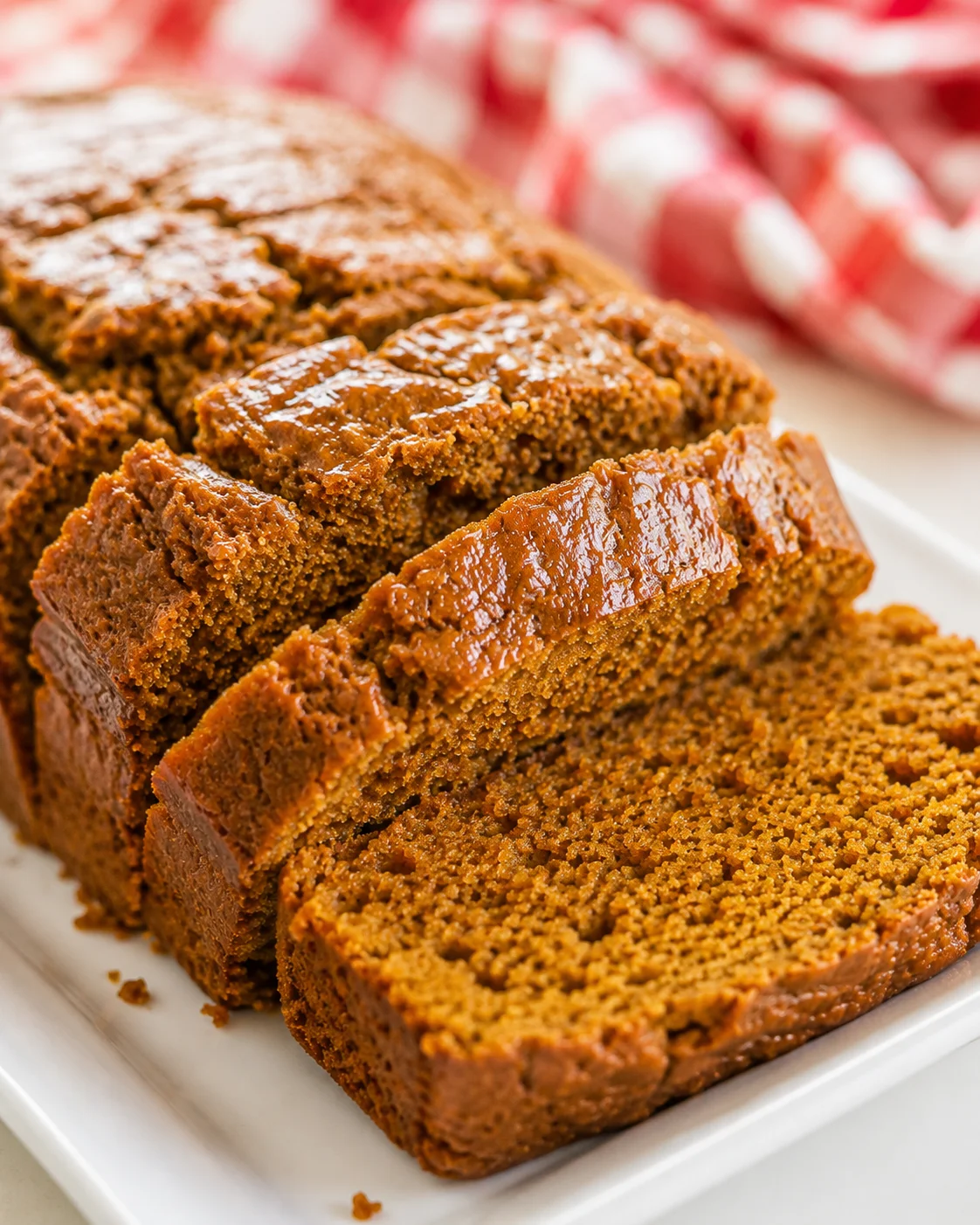 Sliced vegan pumpkin applesauce bread on a white platter with a red check cloth in the background